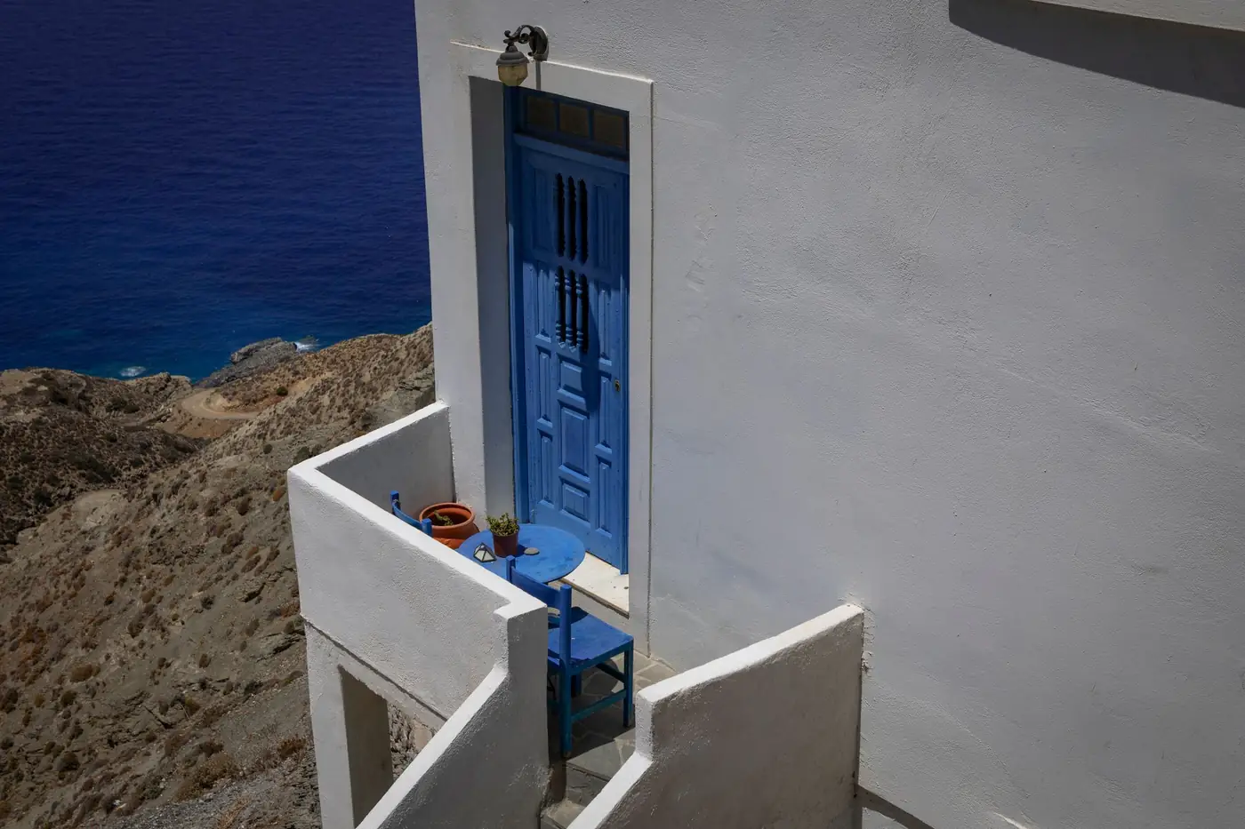 Blauwe deur en balkon van een woning met uitzicht op de Egeïsche Zee