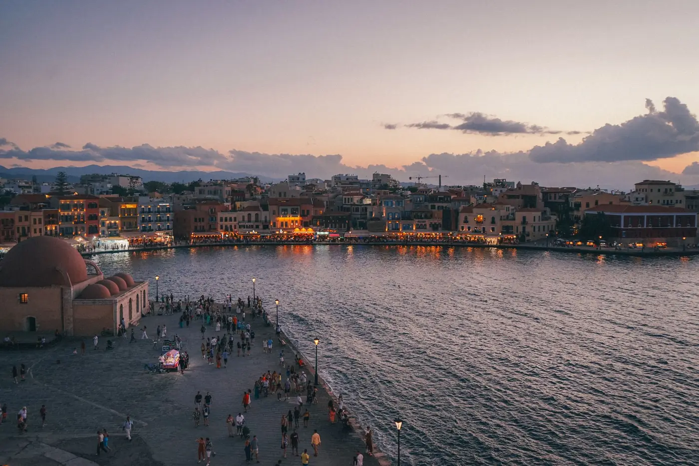 Waterfront van Chania op Kreta bij zonsondergang met wandelaars langs de kade
