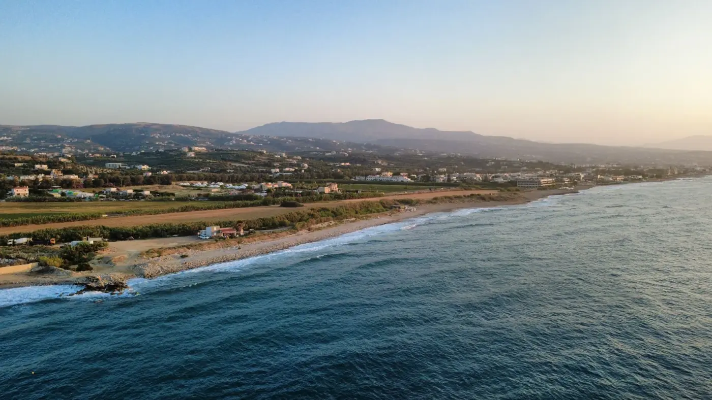 Scenic aerial view of Adelianos Kampos, Greece, showcasing the coastline and distant mountains at sunset.