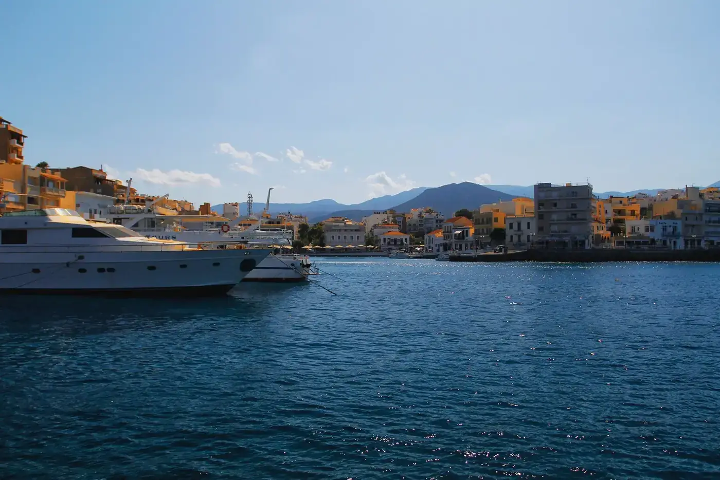 Picturesque harbor with yachts and buildings in Agios Nikolaos, Crete under a clear blue sky.