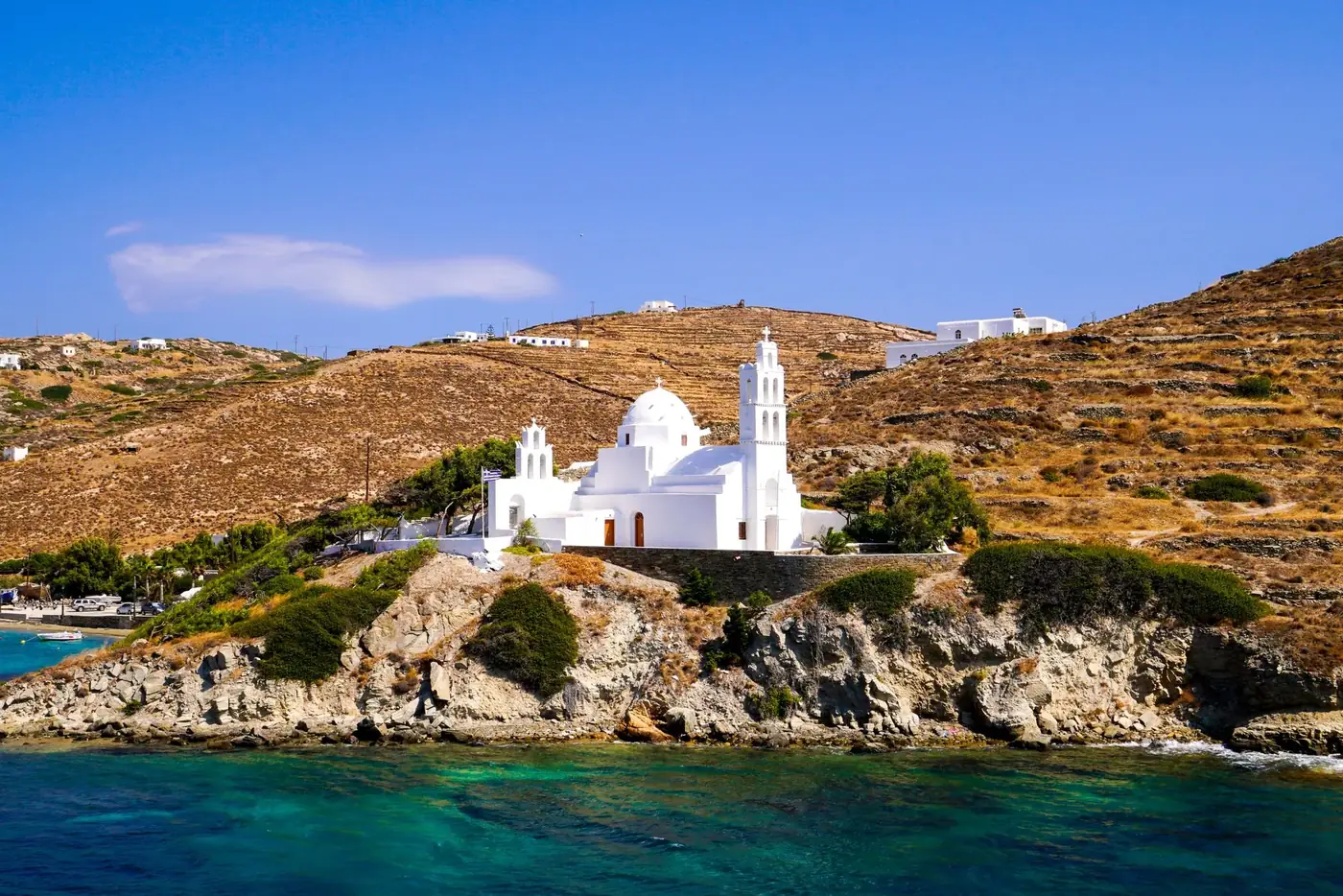 Beautiful white church on a rocky coastline in Greece under a clear blue sky.
