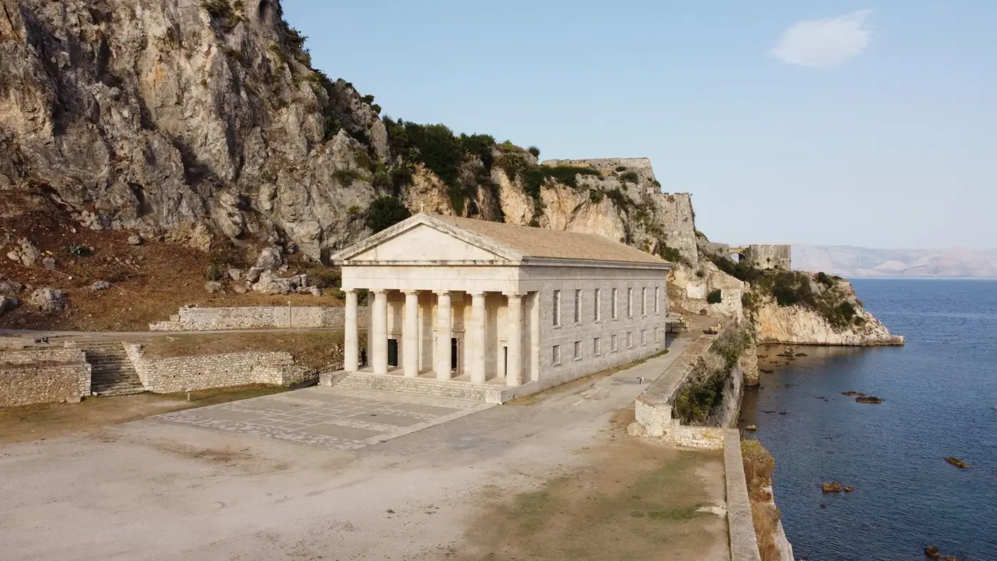 Majestic ancient temple by the sea in Kerkira, Greece, surrounded by rocky cliffs.