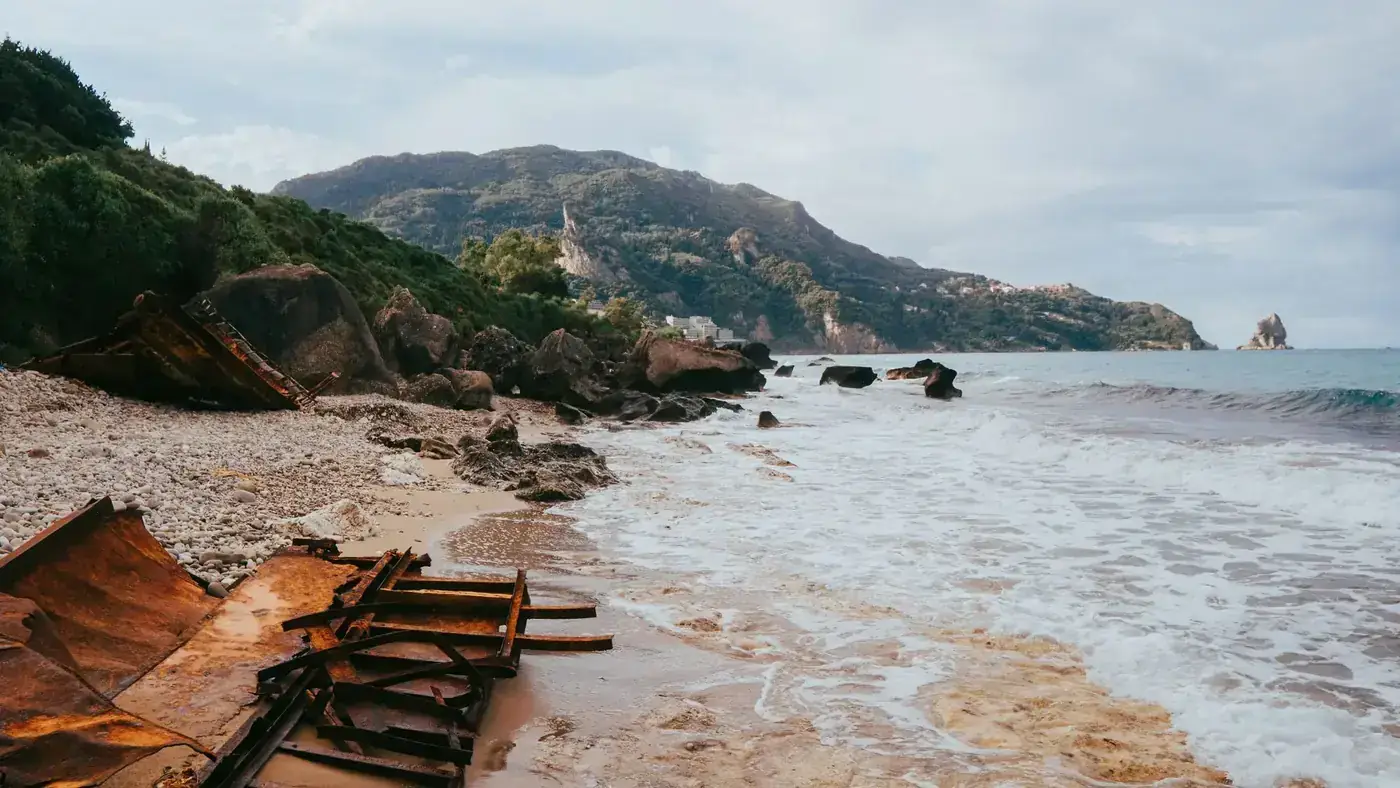 Explore the tranquil beaches of Corfu with a scenic view of a rusted shipwreck along the shore.