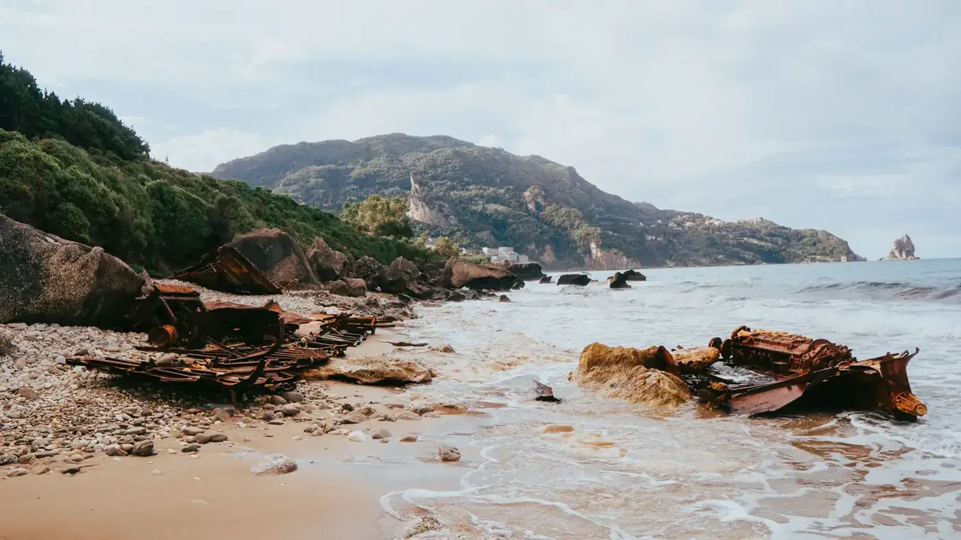 Explore the tranquil Agios Gordios beach featuring a captivating shipwreck and lush surrounding hills.
