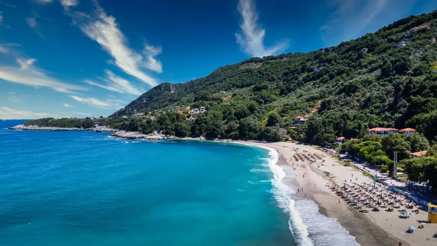 Stunning aerial view of Agios Ioannis beach in Greece, showcasing clear turquoise waters, lush greenery, and mountain ba