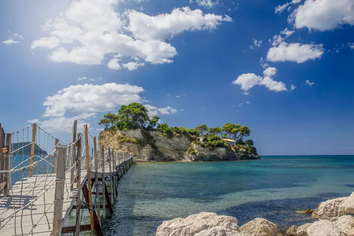 Beautiful wooden bridge leading to a small islet with green trees and clear blue sea in Zakinthos, Greece.