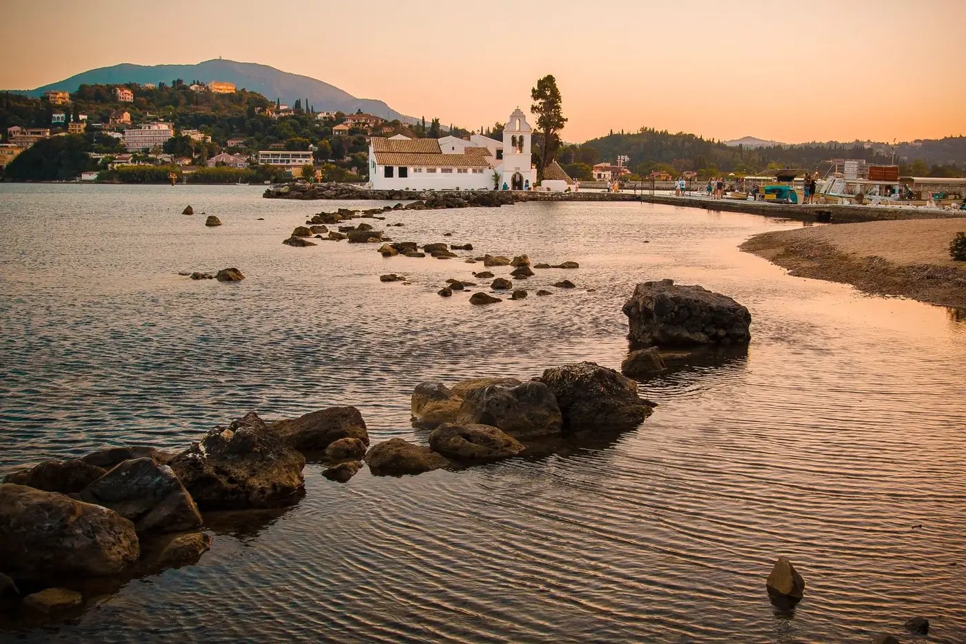 Scenic view of a coastal church during sunset in Corfu, Greece, with rocky shoreline.