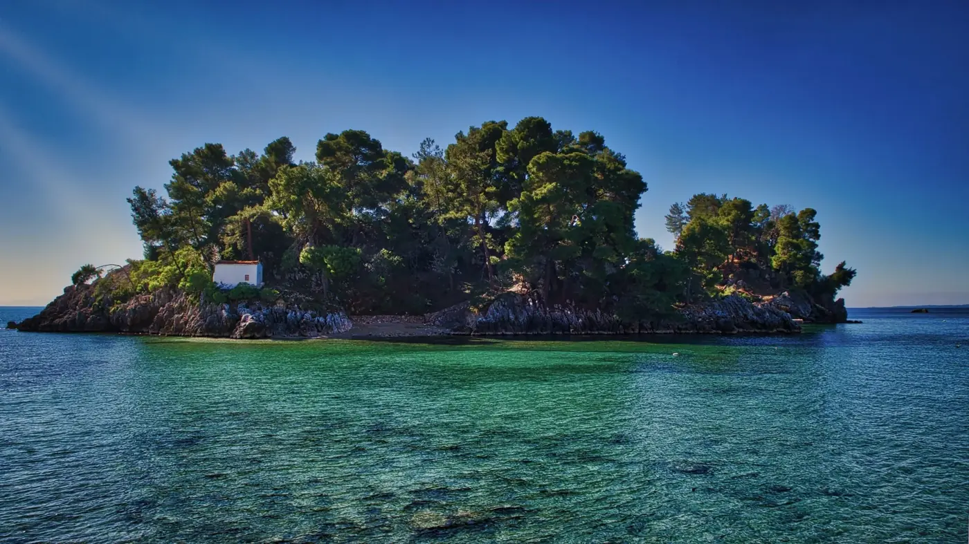 Discover the serene beauty of an untouched Greek island surrounded by clear azure waters and lush green foliage.