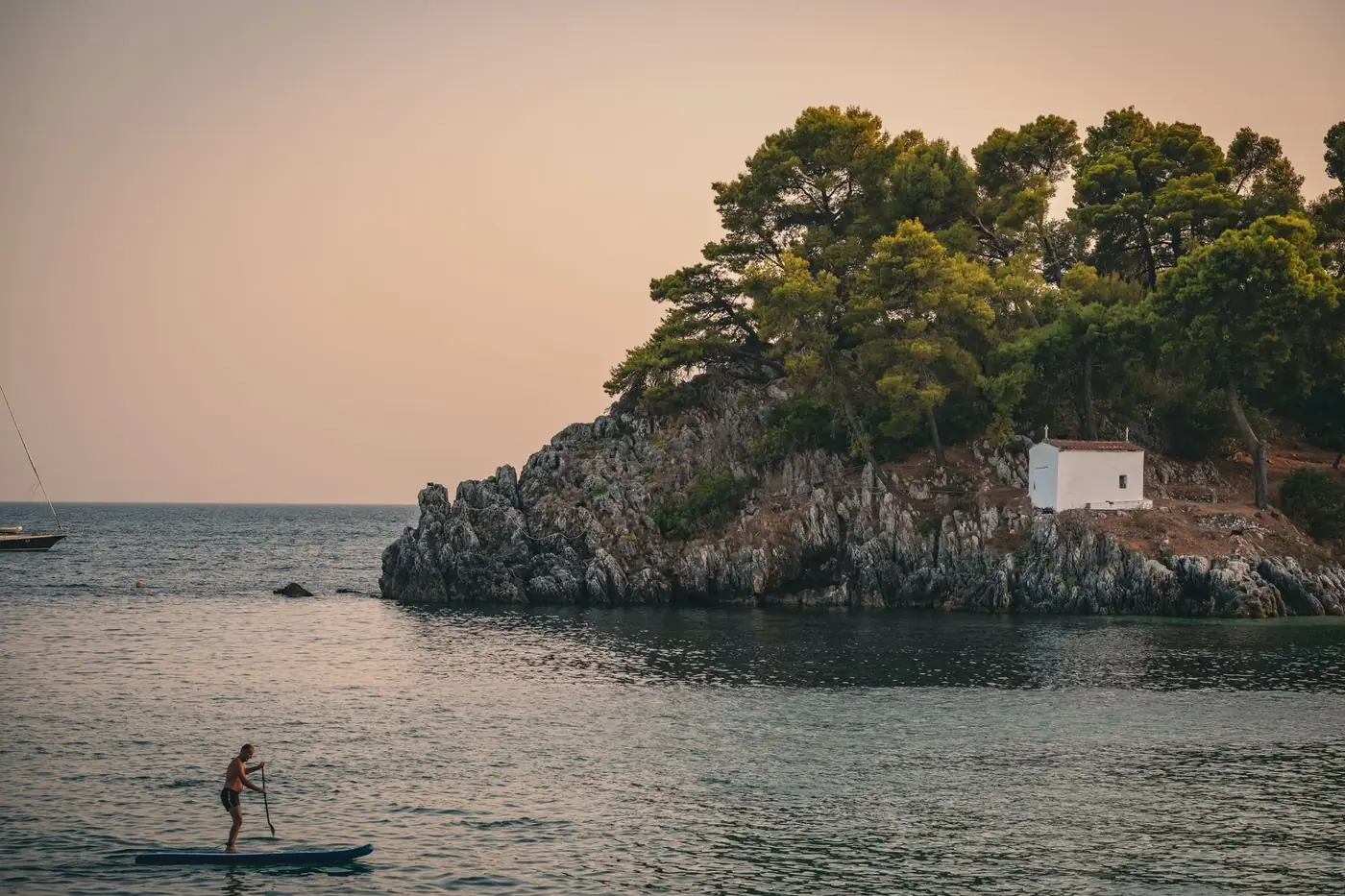A person paddleboarding near a scenic cliffside in Parga, Greece at sunset, showcasing serene coastal beauty.