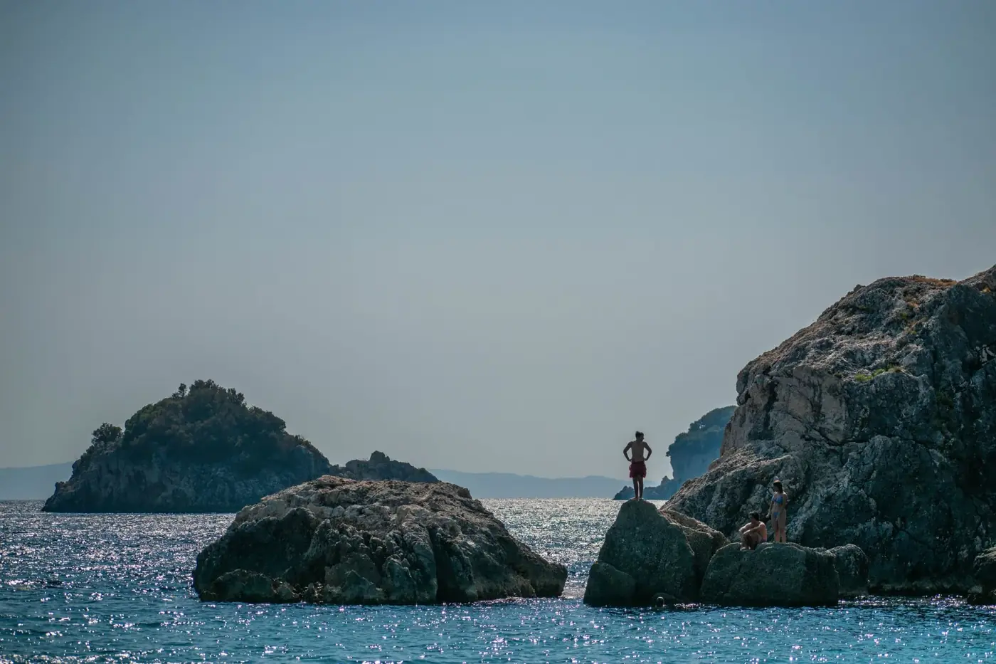 People enjoying the rocky coastline and blue sea in Parga, Greece.