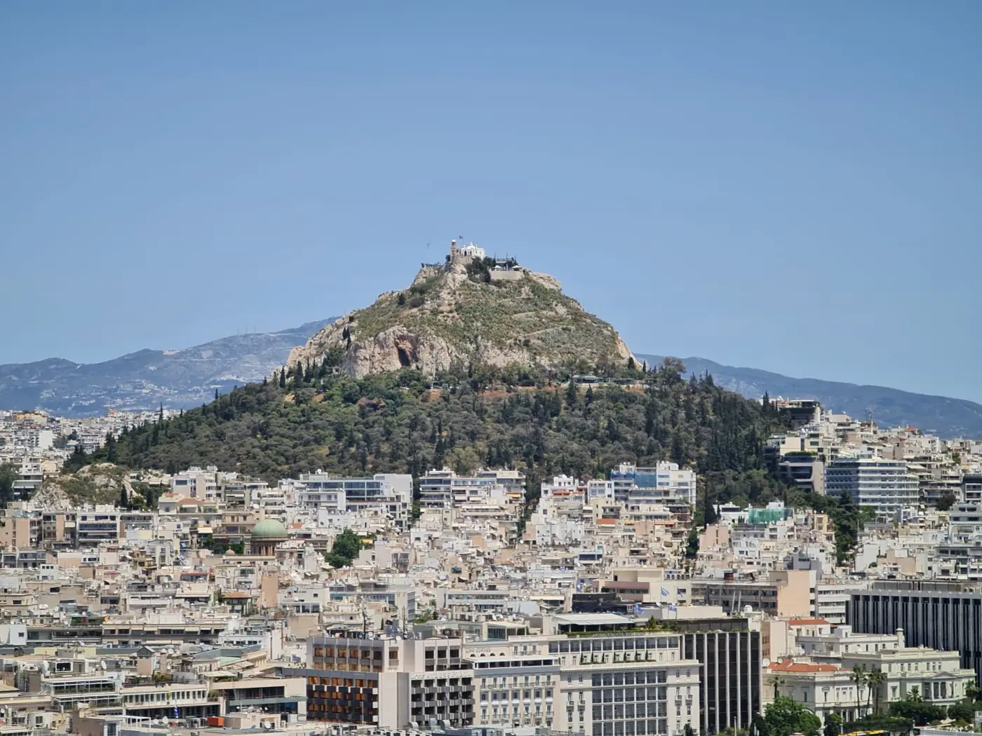 A stunning view of Lycabettus Hill rising above the Athens cityscape under a clear blue sky.