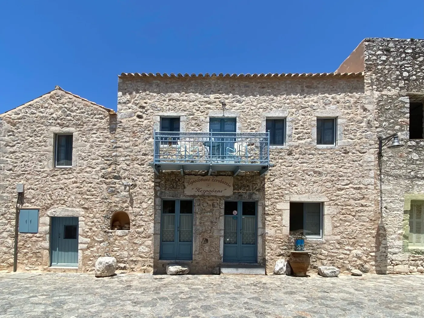 Charming stone house in Mani, Greece, showcasing traditional architecture with a bright blue sky backdrop.