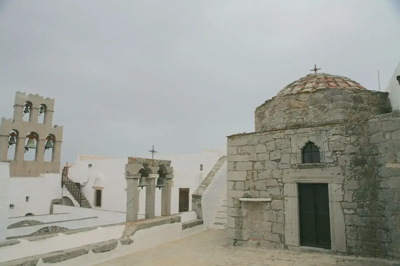 View of a traditional Greek monastery with ancient stone structures and a bell tower.