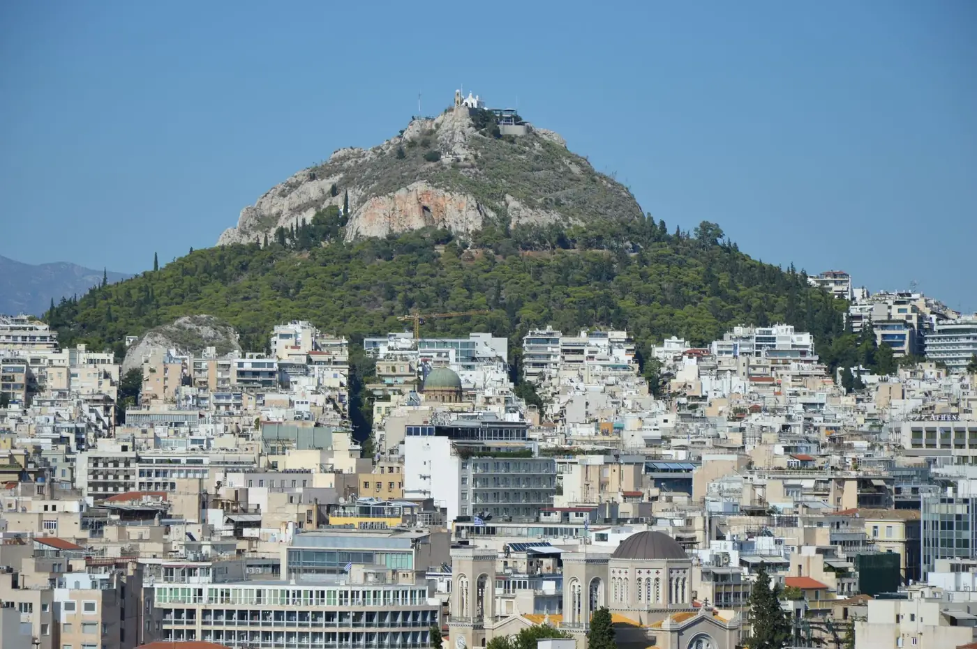 View of Lycabettus Hill and the Athens cityscape under clear blue skies.