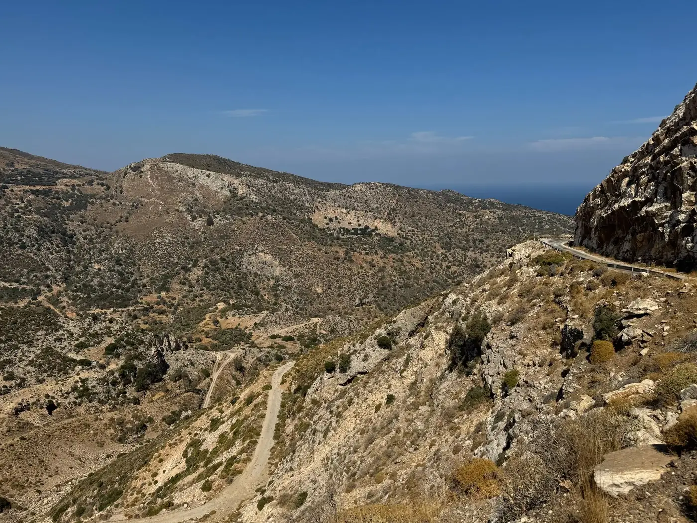 Scenic mountain landscape with rugged terrain and coastal horizon under clear blue sky.