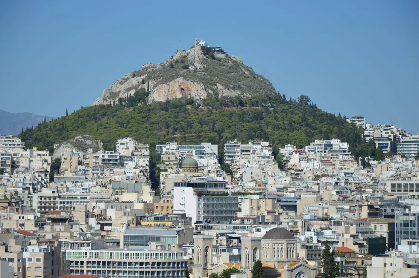 View of Lycabettus Hill and the Athens cityscape under clear blue skies.