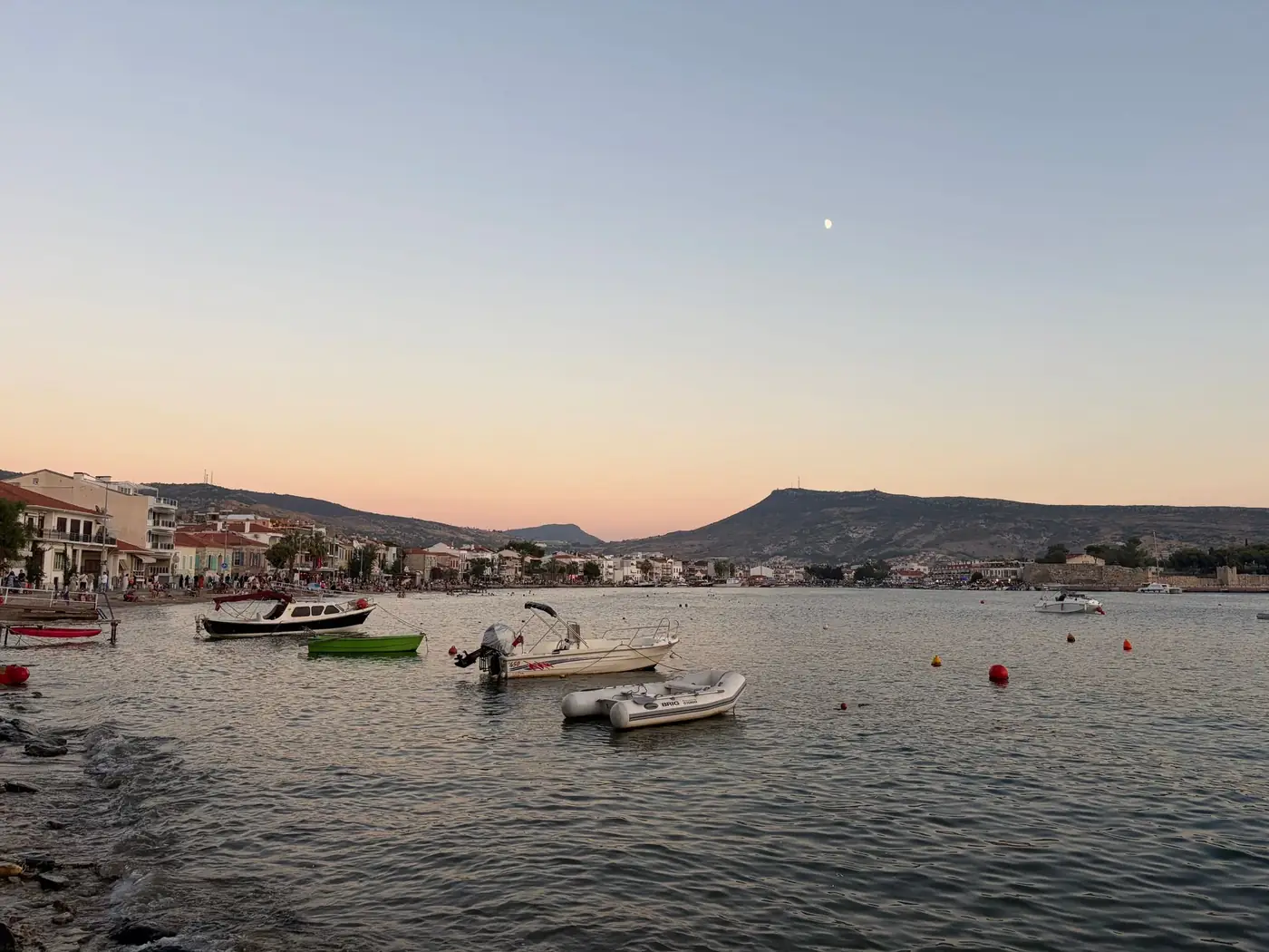 Tranquil sunset over Mytilene harbor, featuring boats and a distant town view under a pastel sky.