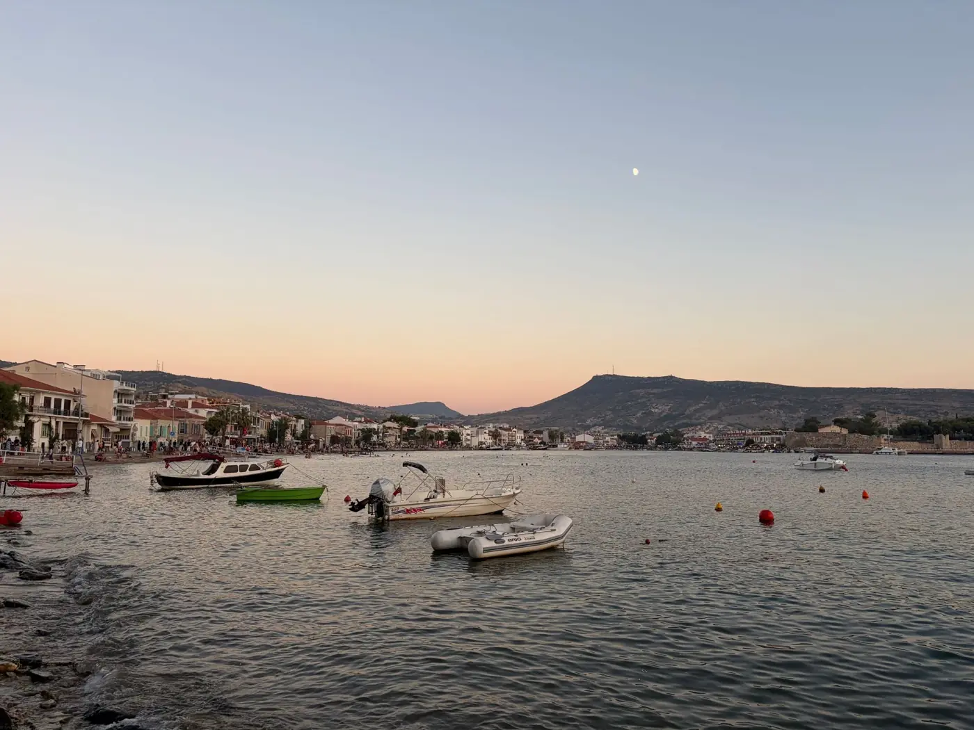 Tranquil sunset over Mytilene harbor, featuring boats and a distant town view under a pastel sky.