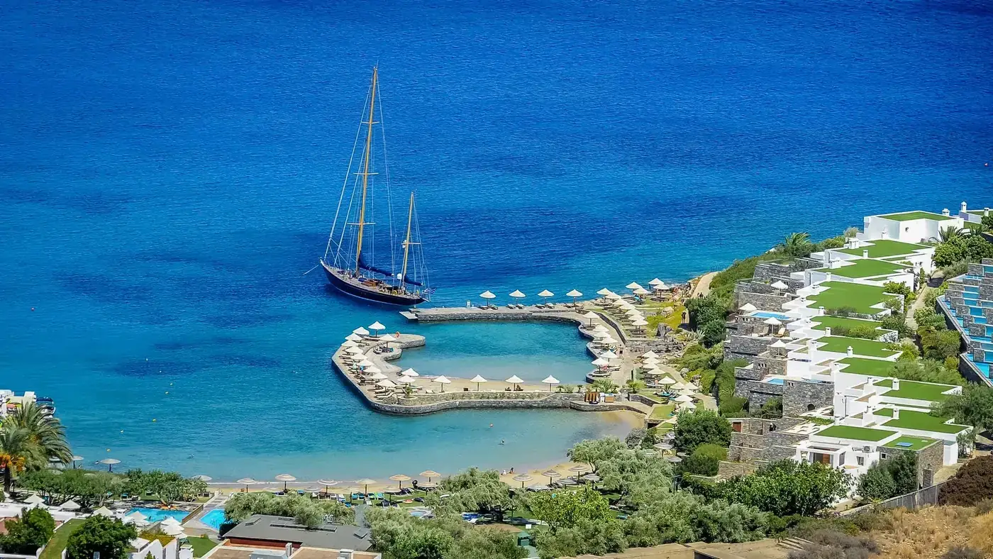 Aerial view of a luxury yacht docked at a resort with vibrant blue waters in the Mediterranean.