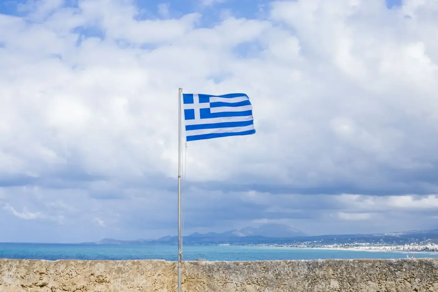Vibrant Greek flag waving on a flagpole against the scenic Mediterranean seascape.