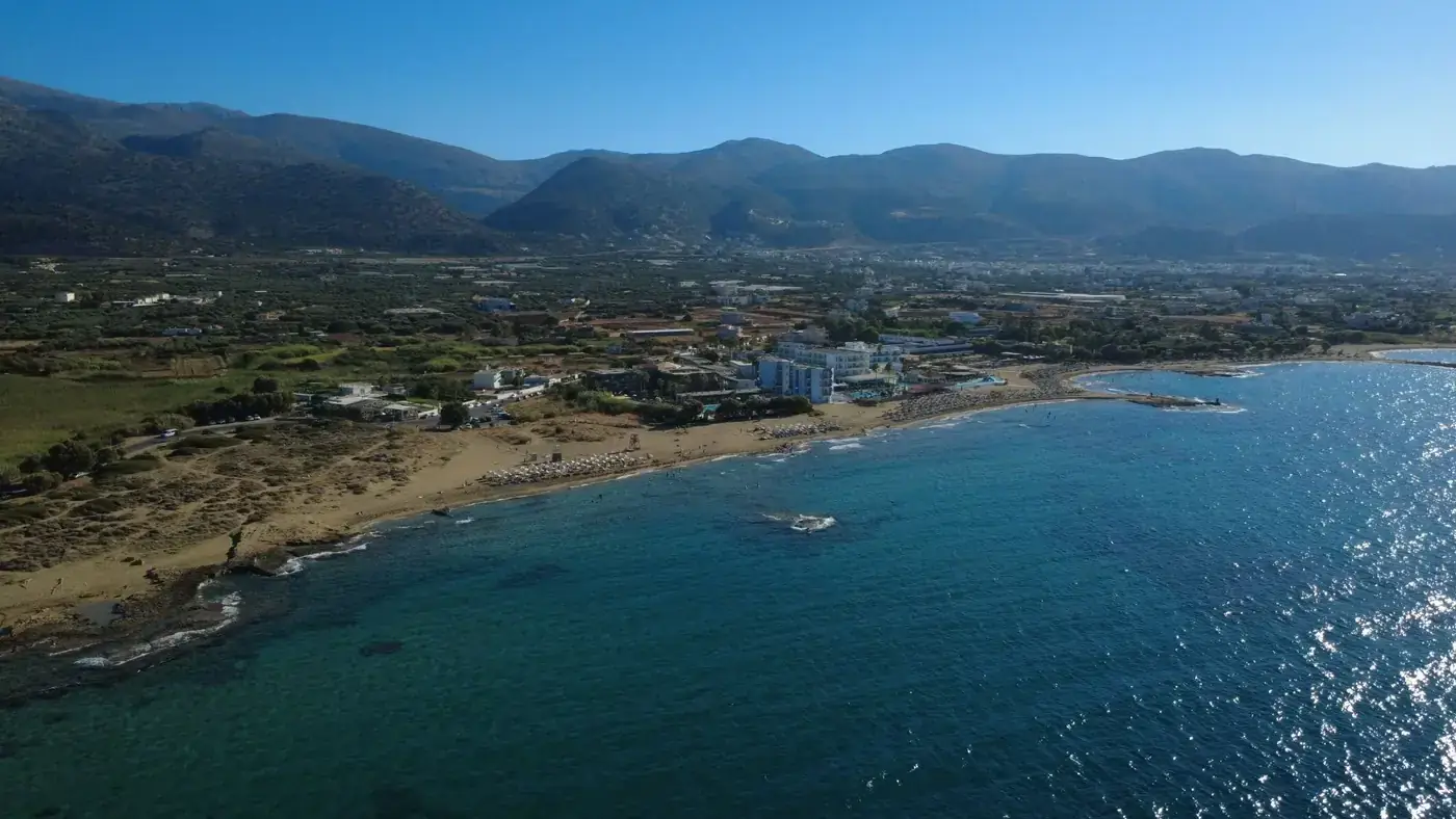 Stunning aerial shot of Malia beach with majestic mountains and clear blue waters in Greece.