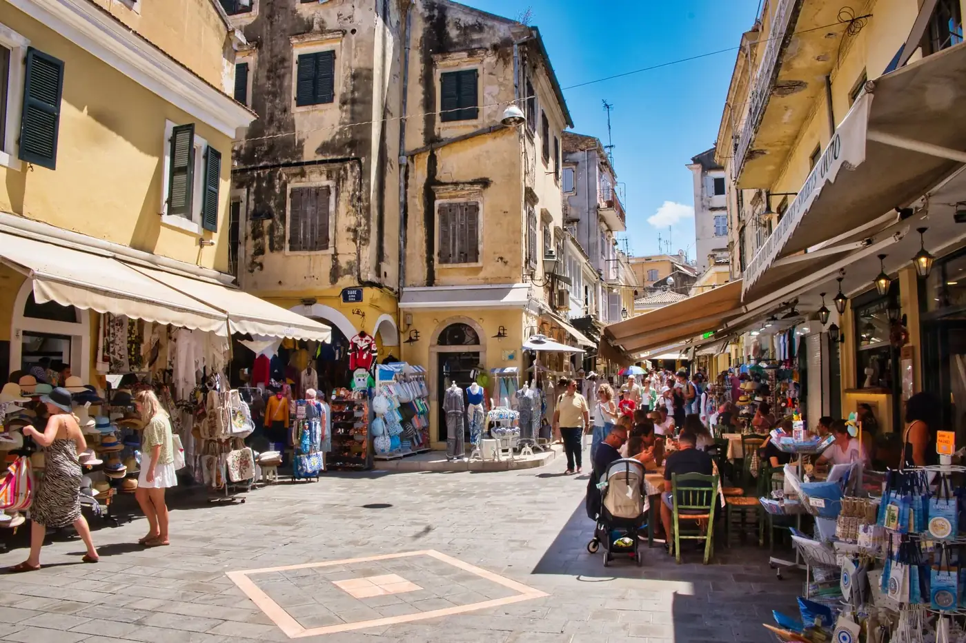 Vibrant street scene in Corfu Town, Greece, showcasing local shops and cafes under sunny skies.