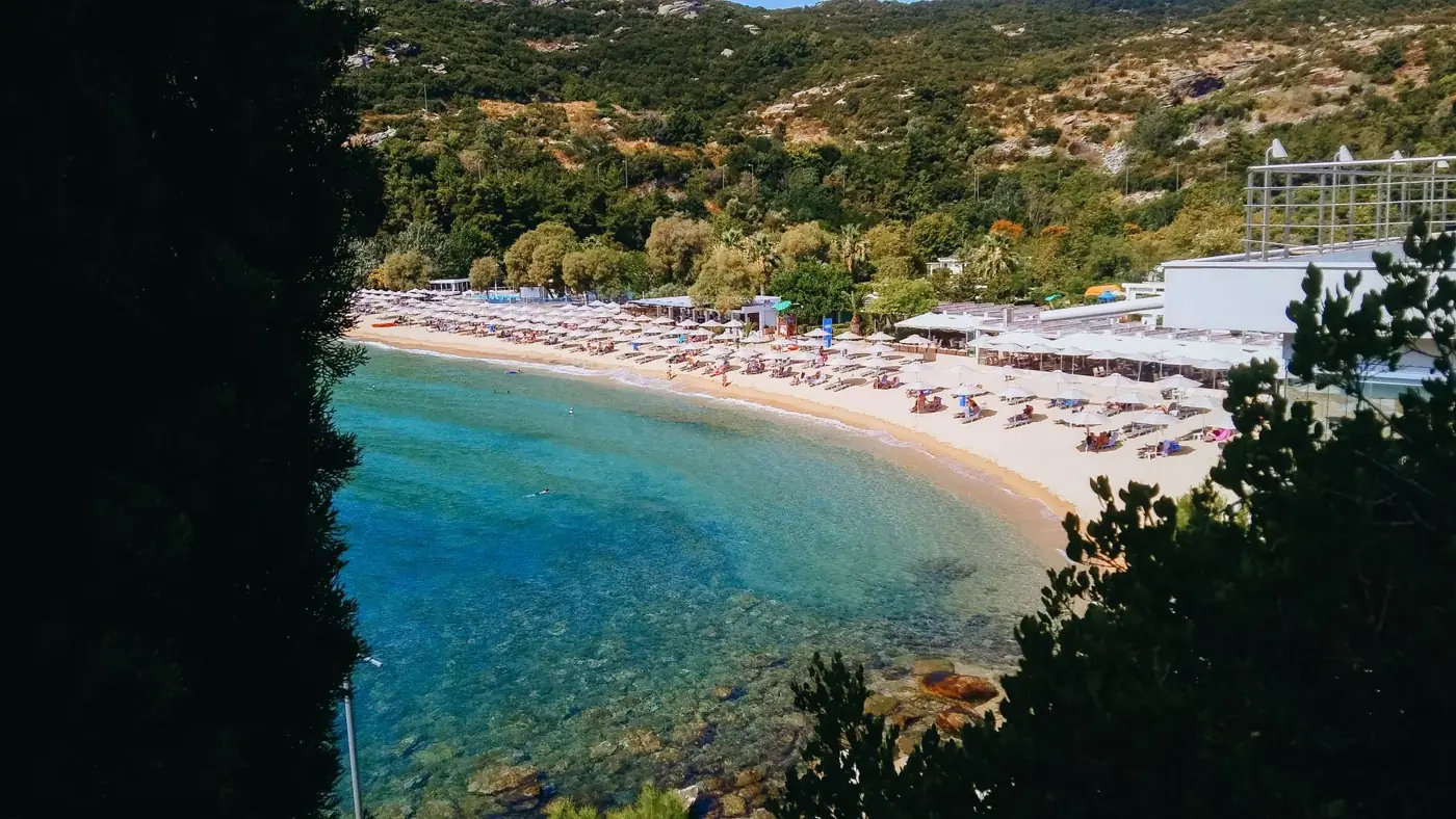 A vibrant seaside resort featuring a sandy beach with umbrellas and lush greenery.