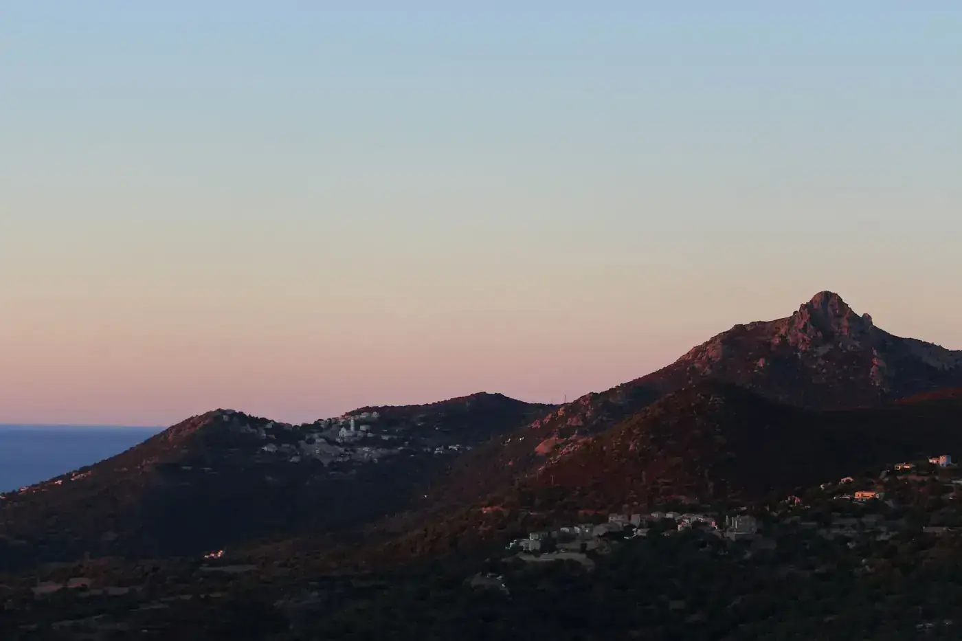 Picturesque scenery mountains with little settlement located against cloudless sky with sea in distance in evening time 