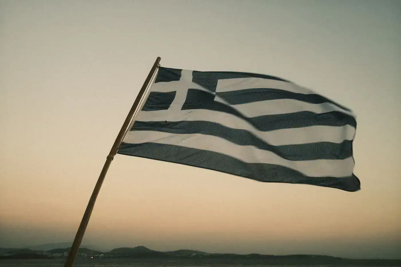 A Greek flag waving against a serene sunset sky in Athens, Greece.