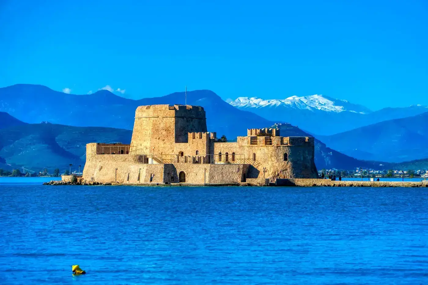 Beautiful daytime view of Bourtzi Castle in Nafplio, Greece, with mountains and sea.
