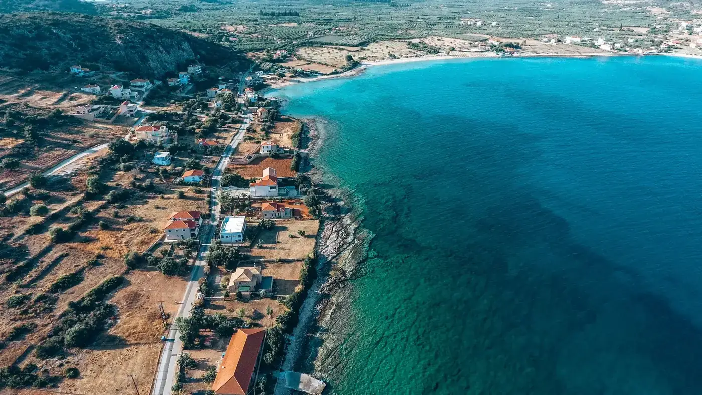 A stunning aerial shot capturing the coast of Plitra, Greece with vibrant blue waters and houses lining the seashore.
