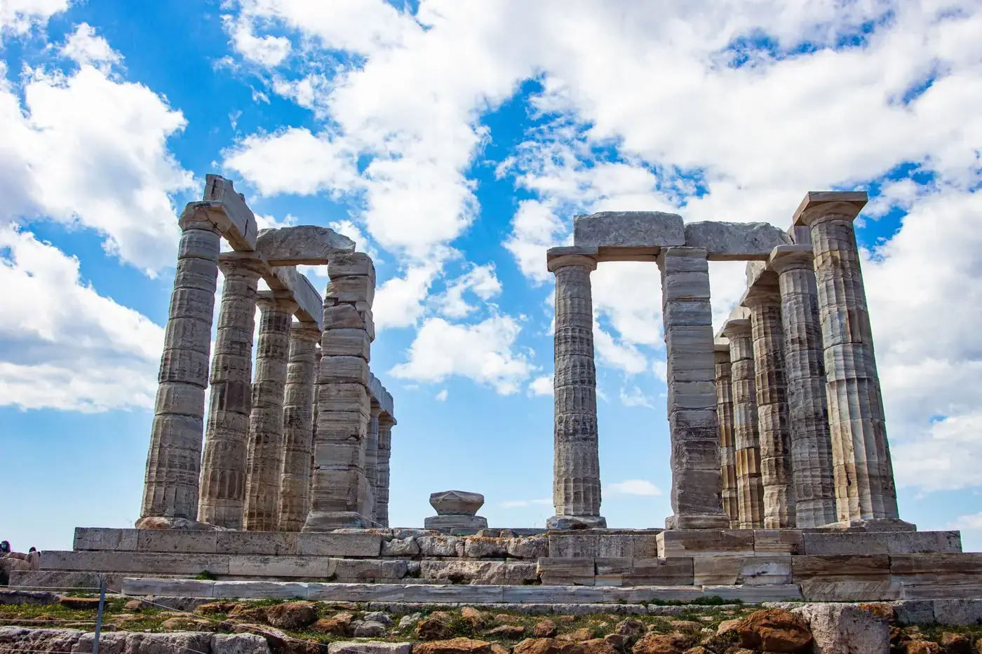 Stunning daytime view of the ancient Temple of Poseidon against a bright blue sky with fluffy clouds.