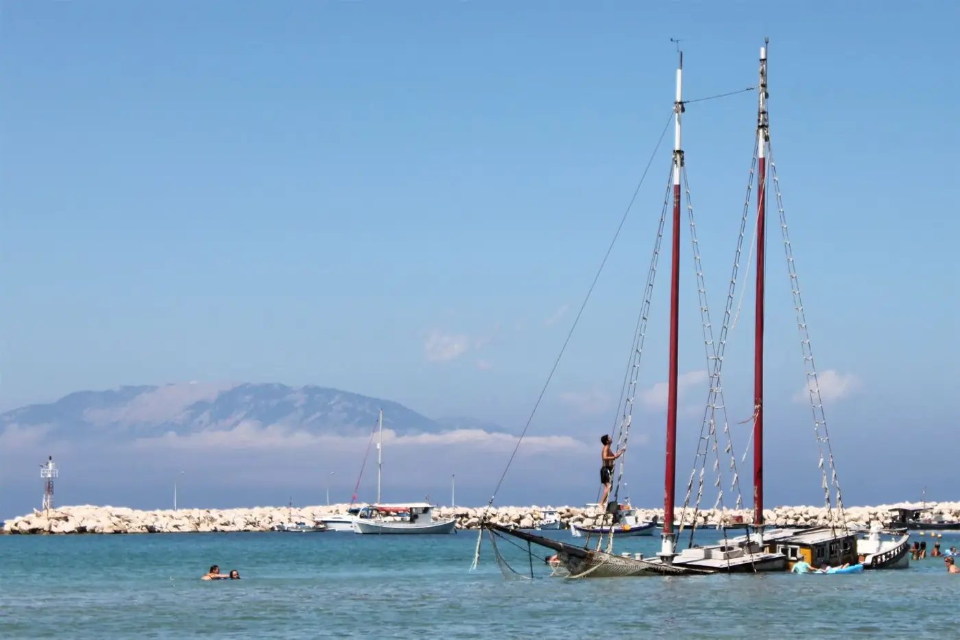 Enjoy a sunny day at Zakinthos harbor with sailboats and swimmers.