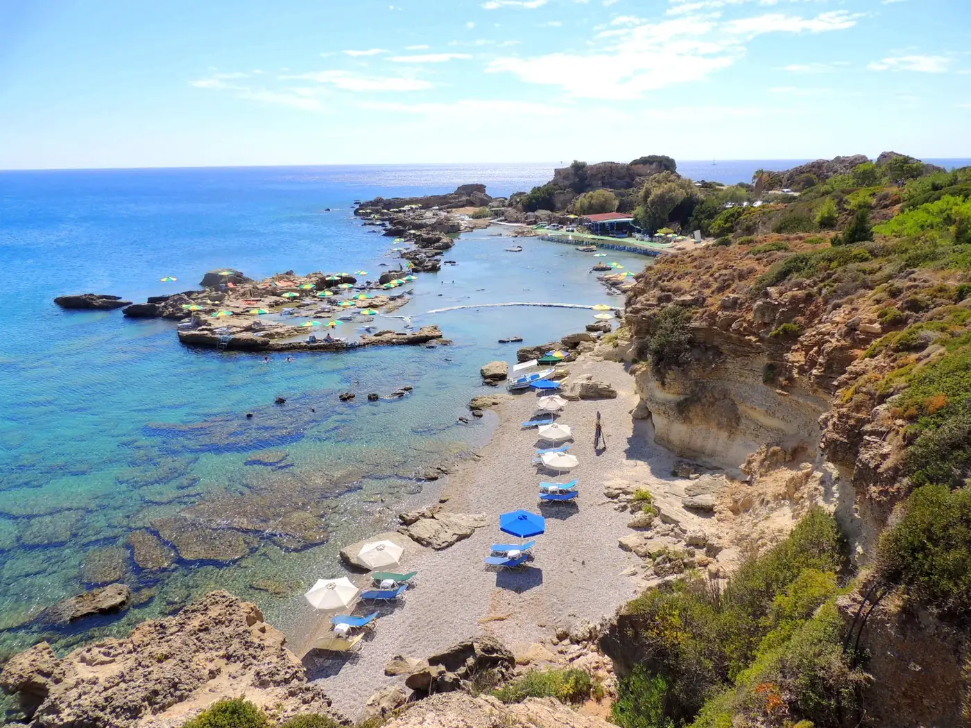 A picturesque coastal scene in Rhodes, Greece, featuring sunlit beaches and clear blue waters.