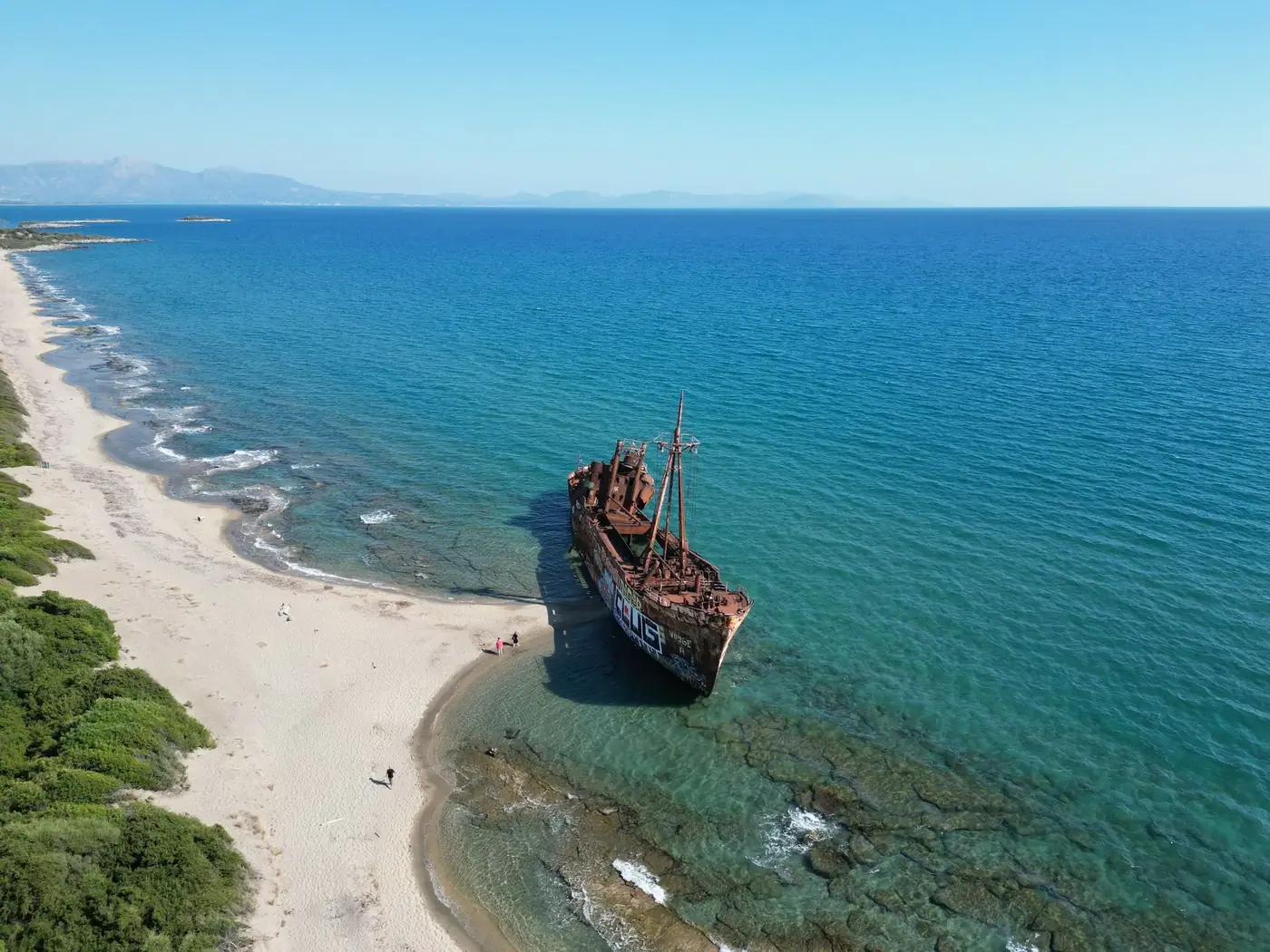 Drone view of a rusty shipwreck on Valtaki Beach, Greece, against the clear blue sea.