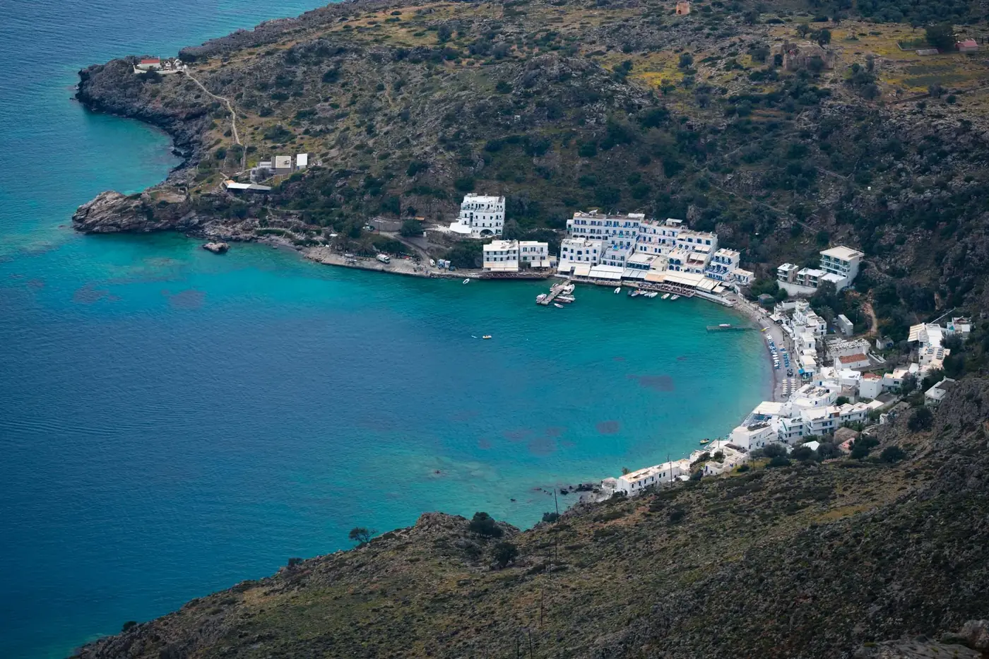 A stunning aerial view of a picturesque coastal village in Greece with turquoise waters and white buildings.