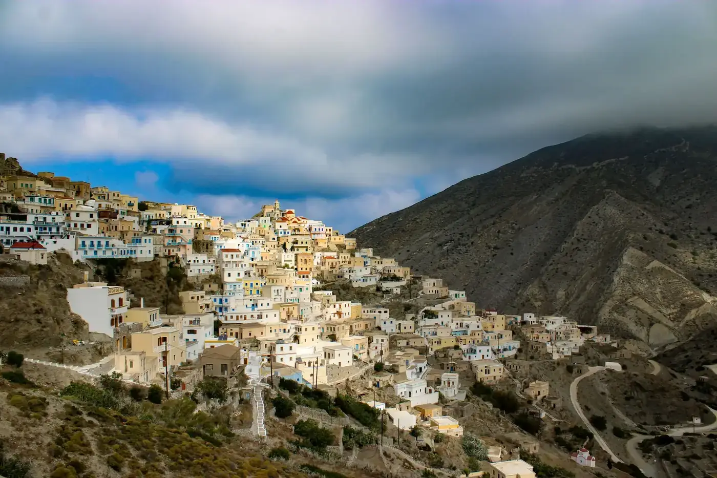 Charming mountain village with traditional houses nestled against a rugged hillside under dramatic clouds.