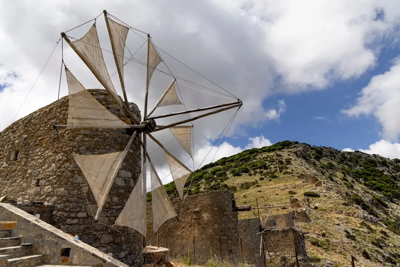 A historic windmill on a hillside in Psichro, Greece under a bright blue sky.