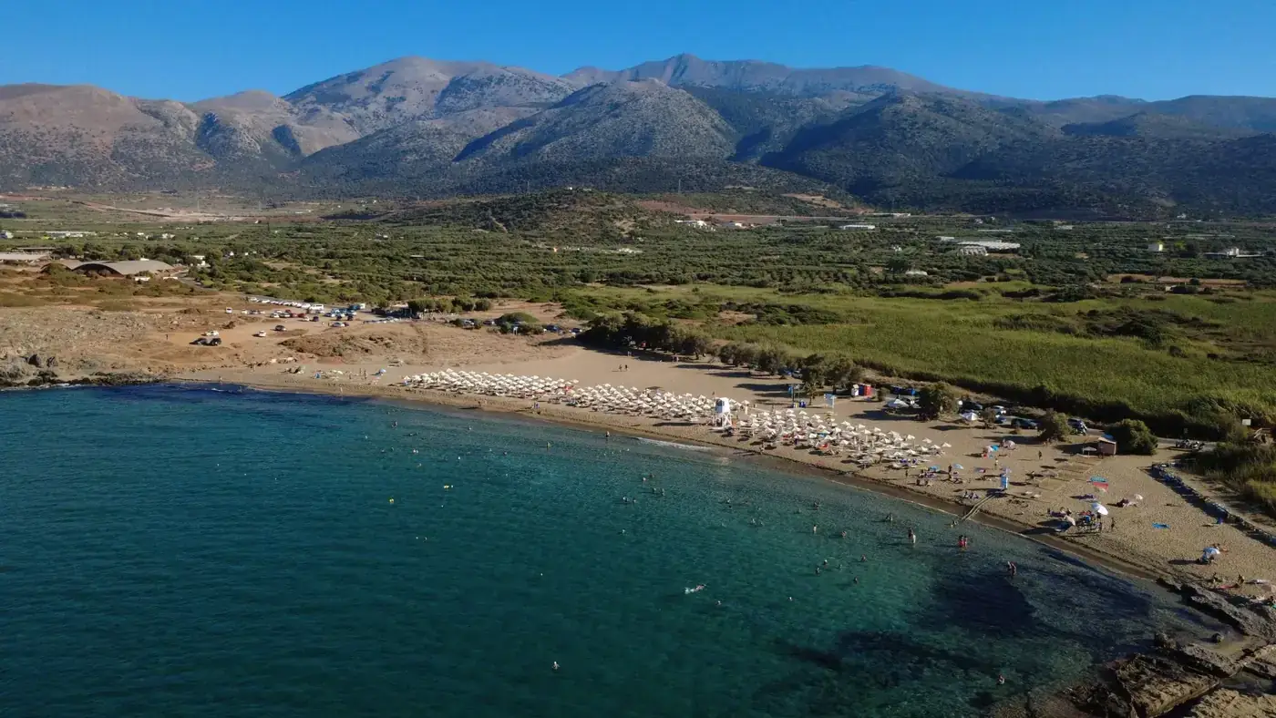 A stunning aerial view of Malia Beach in Crete, Greece, featuring sunbathers and turquoise waters.