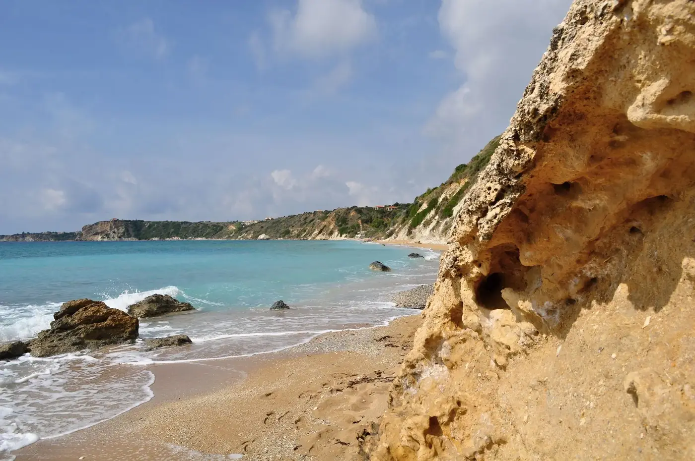 Sunlit rocky shore of Avithos Beach in Greece with turquoise waters and clear sky.