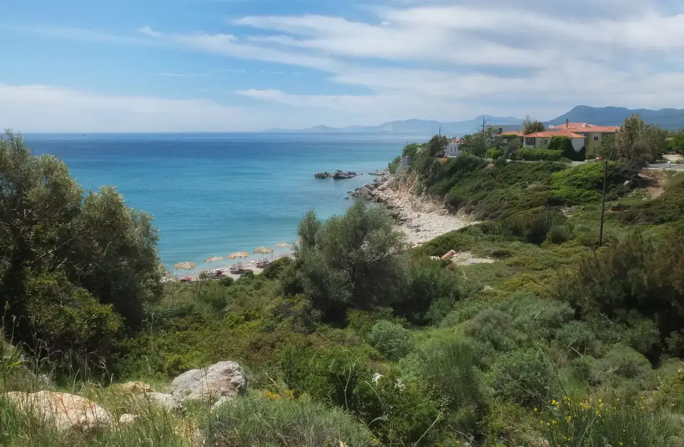 Picturesque view of Samos coastline with clear blue sea, lush greenery, and beach umbrellas.
