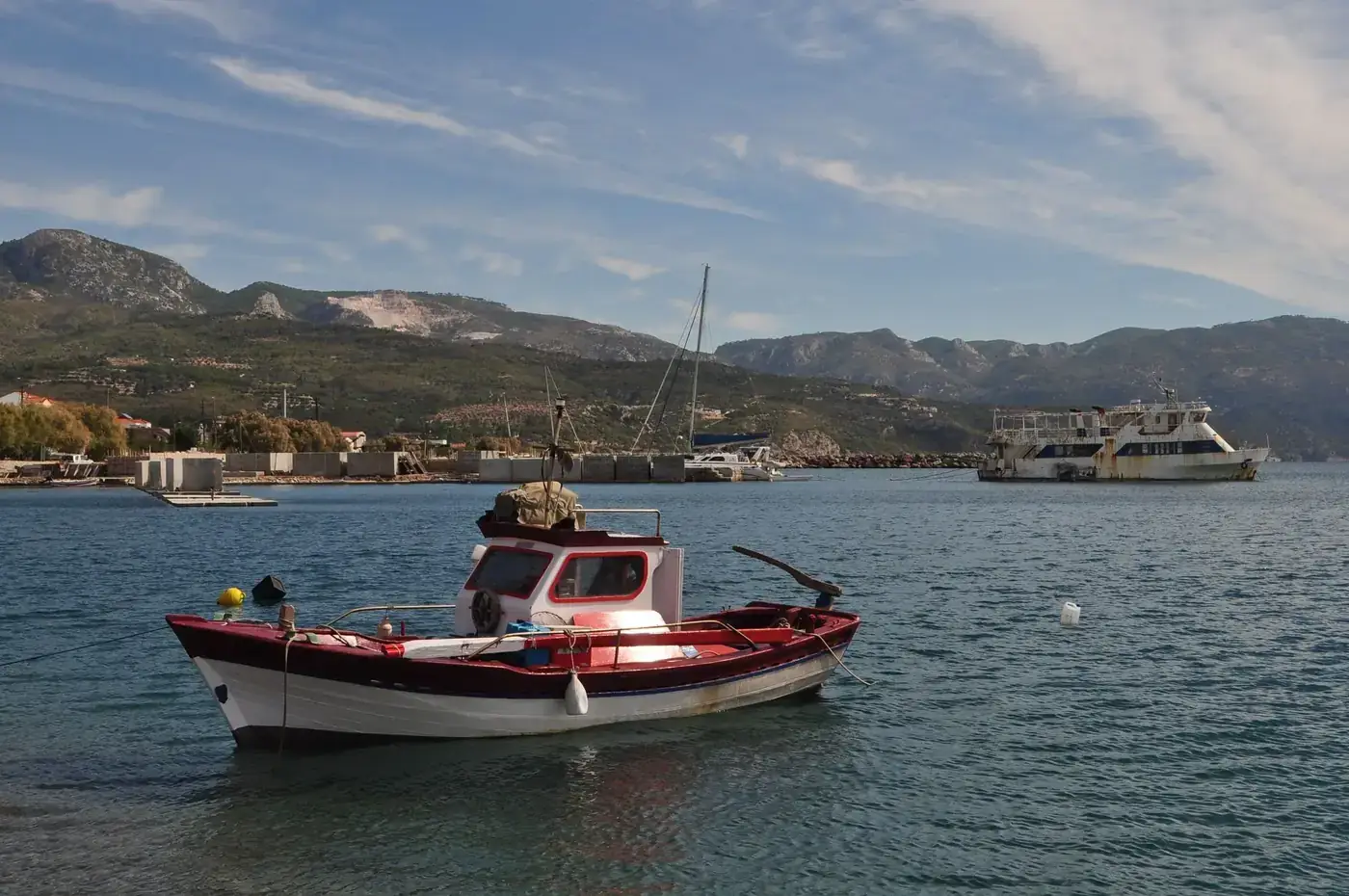 A peaceful fishing boat floating on the calm waters of Samos, Greece, with a scenic mountain backdrop.