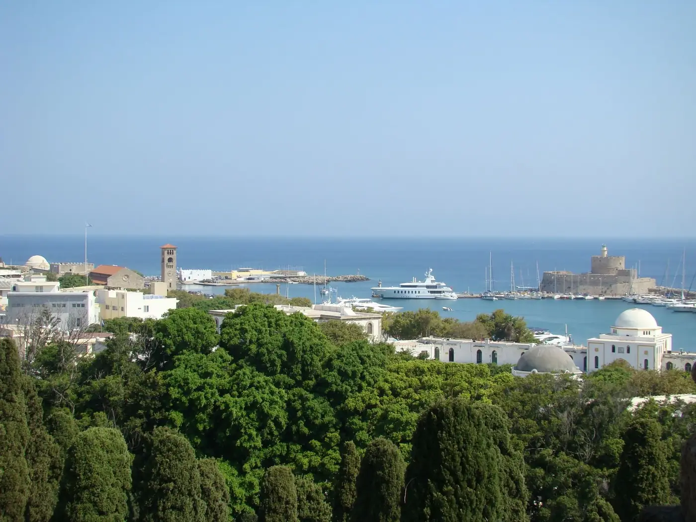 Aerial view of Mandraki Harbor in Rhodes, showcasing boats, greenery, and historical architecture.