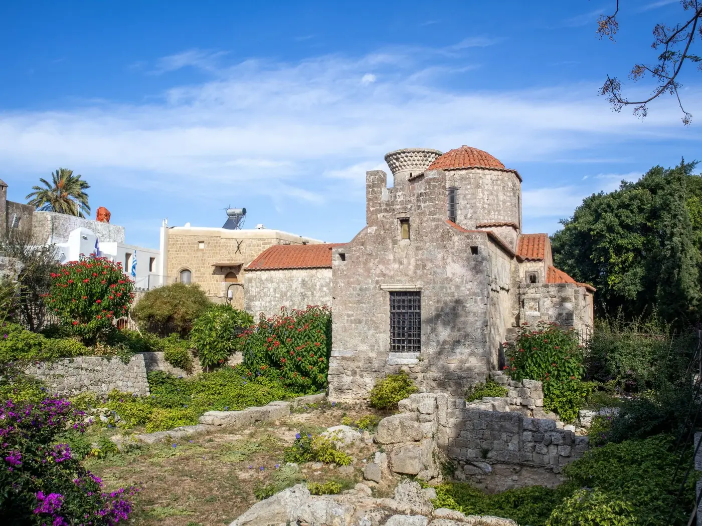 Beautiful historic stone building with lush garden under a clear blue sky, capturing Mediterranean architecture.