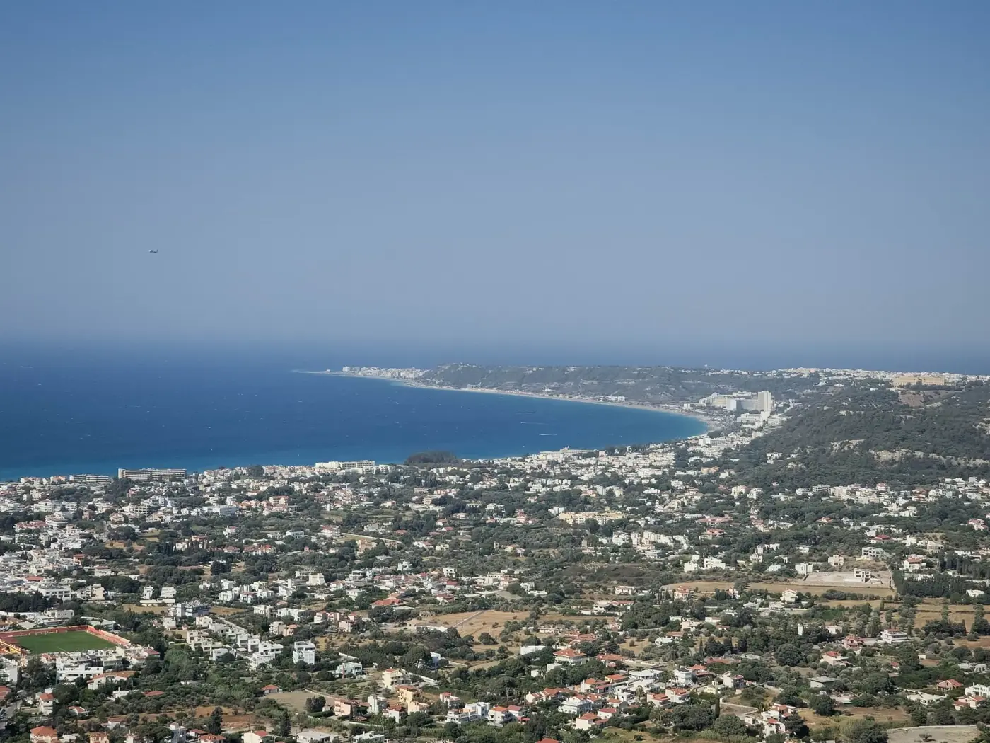 Stunning aerial view of a coastal cityscape and azure sea in Greece on a sunny day.