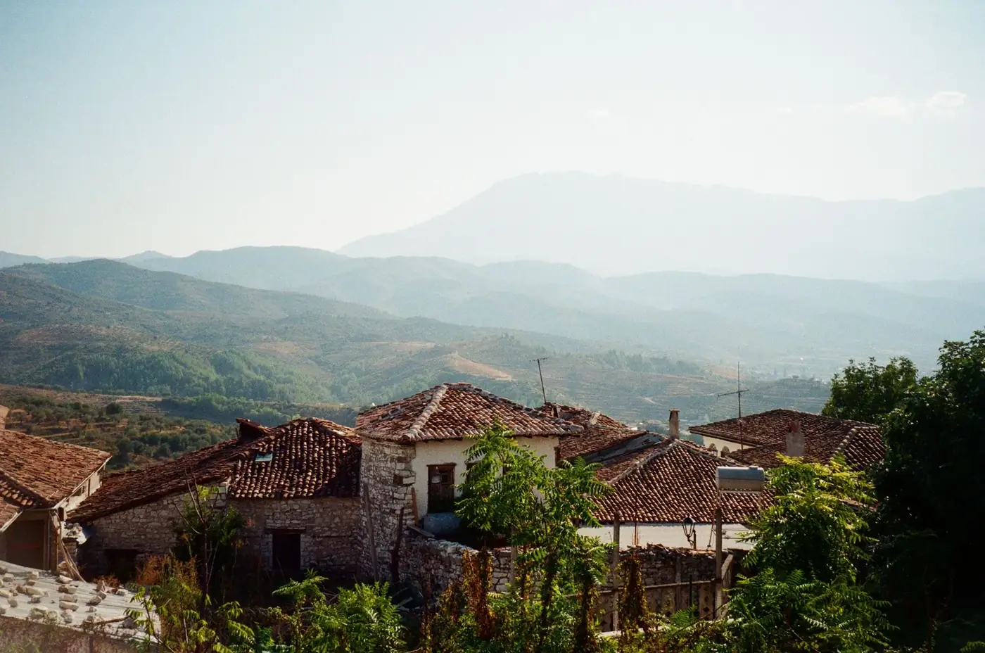 Tranquil rural scene featuring rustic houses with tiled roofs against mountainous backdrop.