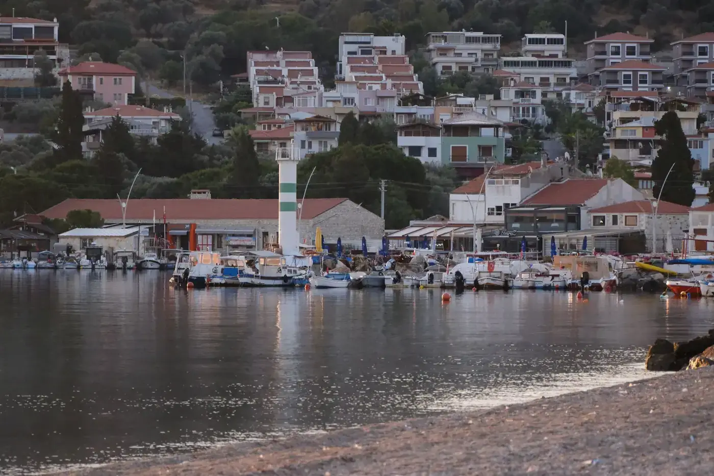 Serene harbor scene in Foça, İzmir with boats and hillside houses at dusk.