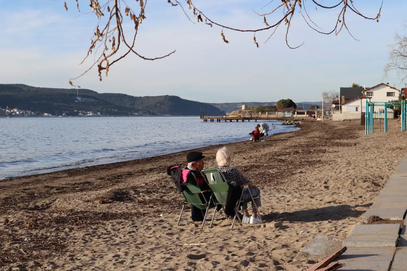 Elderly couple relaxes by the sea on a quiet beach under a clear sky.