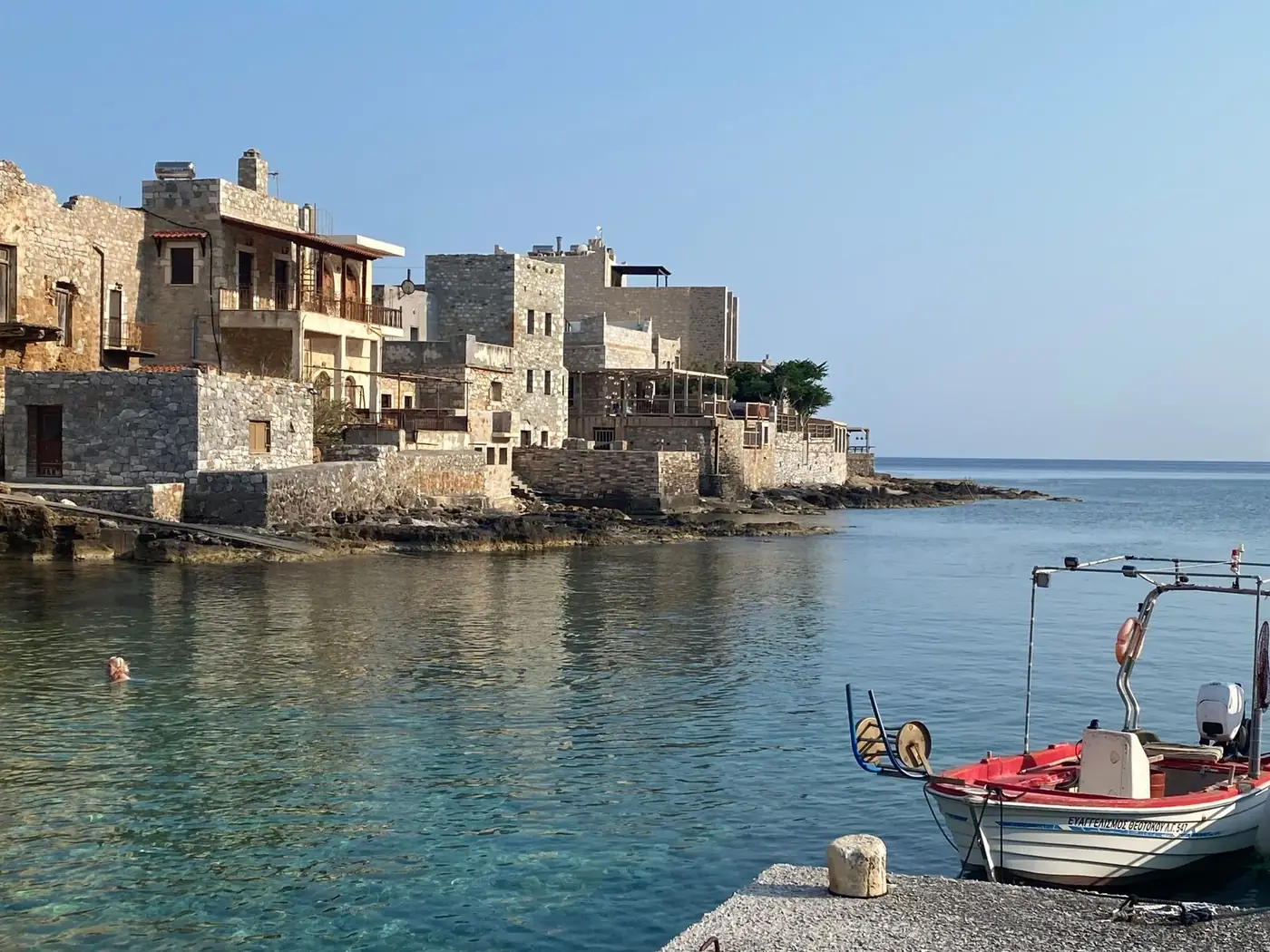 Rustic stone buildings by the sea in a serene Greek coastal village with a small fishing boat.