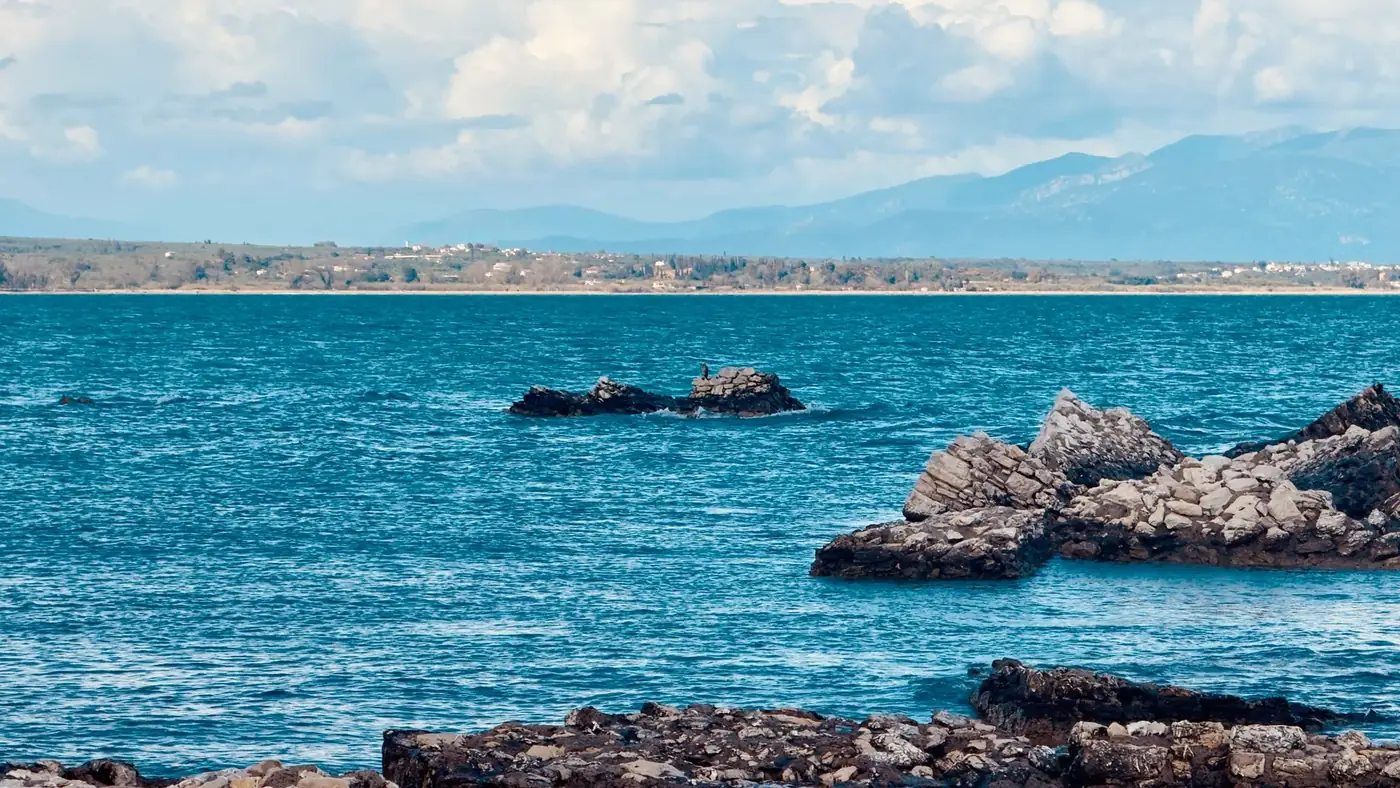 Tranquil seascape with rocky shore and distant mountains in Πεταλίδι, Greece.